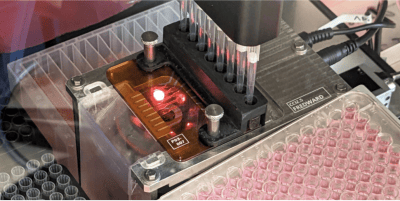 Photo of the automated cell culture passaging system, showing a multi-well plate loaded into a robotic liquid handler with a red-lit cell counting module and pipette tips above.