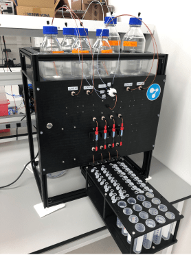 Photo of the four-channel automated chromatography platform, with reagent bottles on top, a valve manifold, and a fraction collector rack of tubes below.