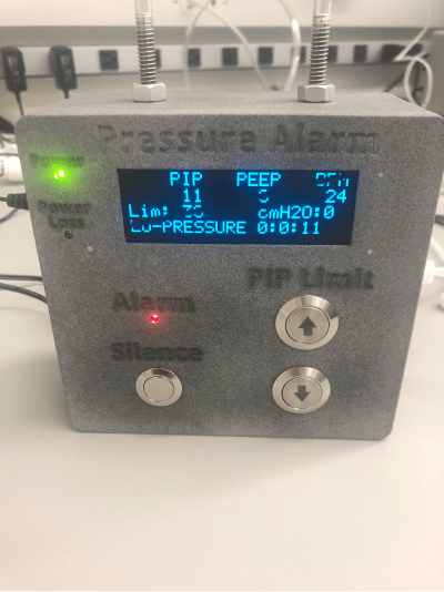 Photo of the ventilator pressure alarm device, showing a digital display with PIP, PEEP, and pressure readings, alarm silence button, and PIP limit dial.