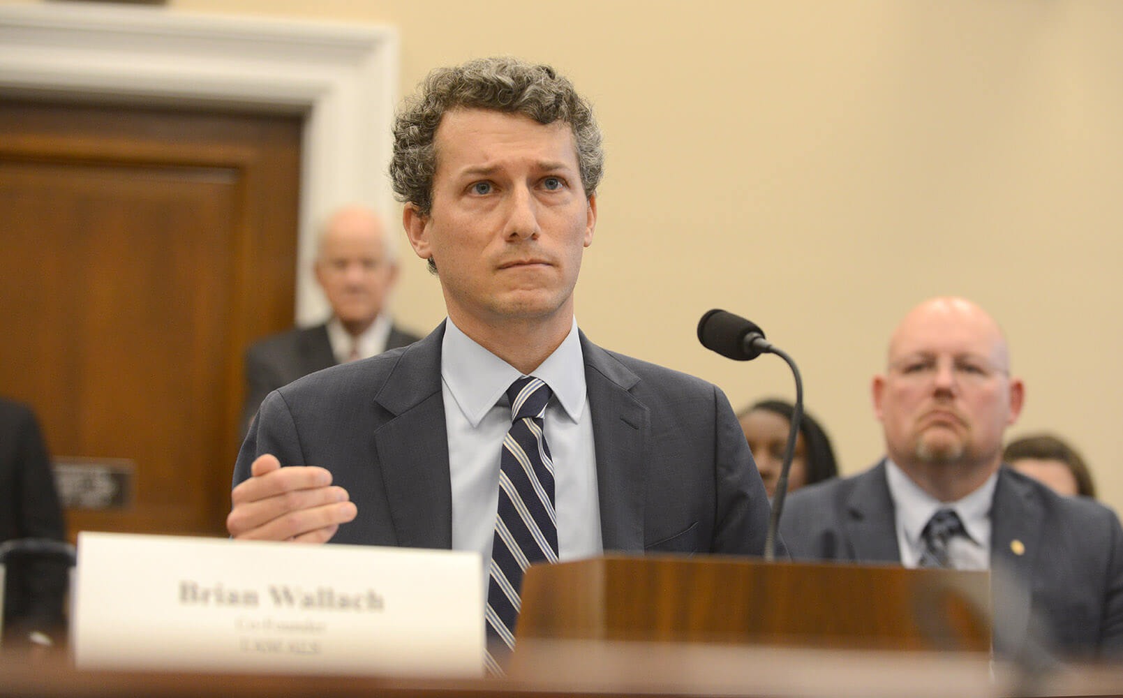 A man sits in front of a microphone and gestures with his hand.