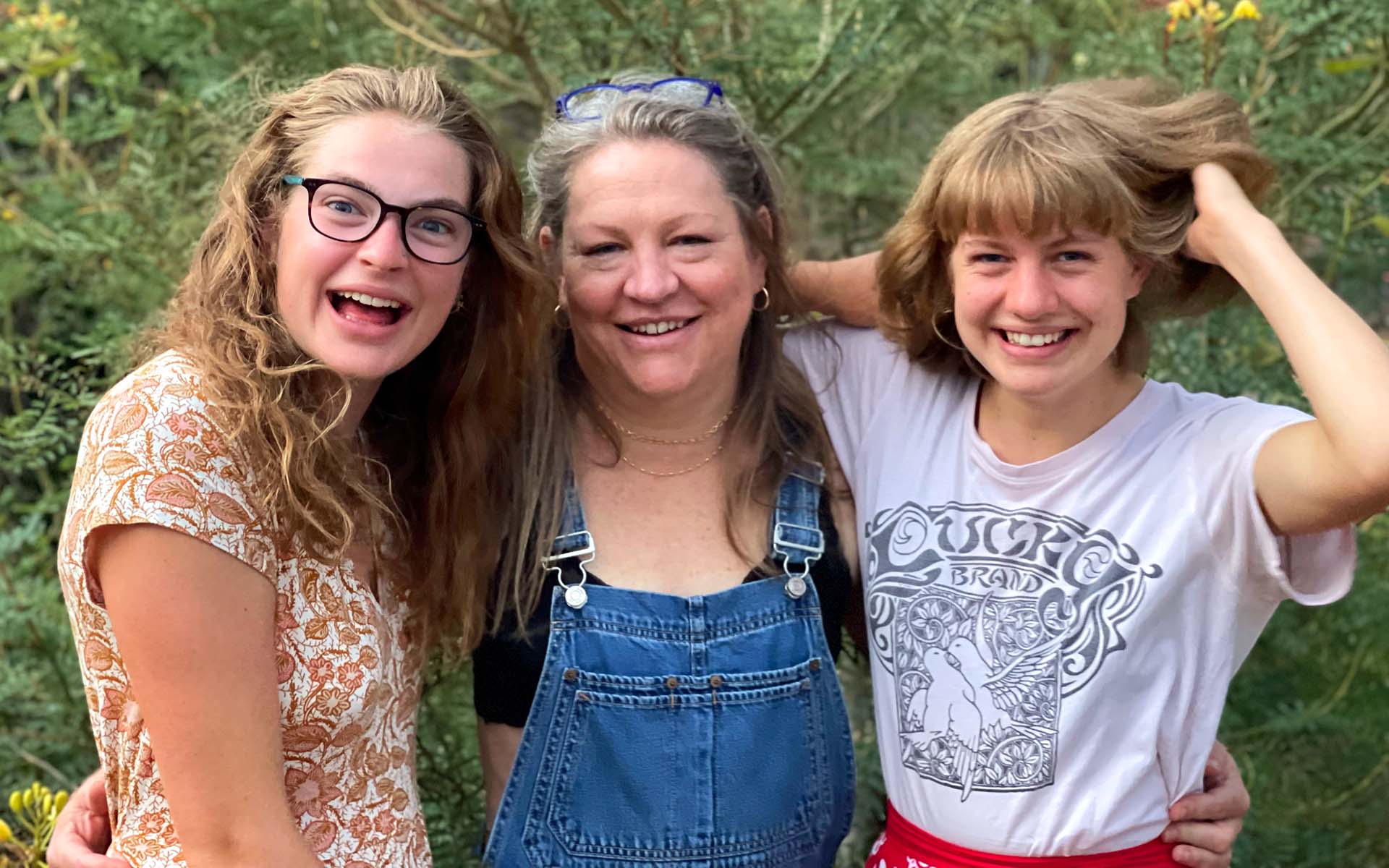 A mother smiling with her daughters smiling and standing on either side of her.