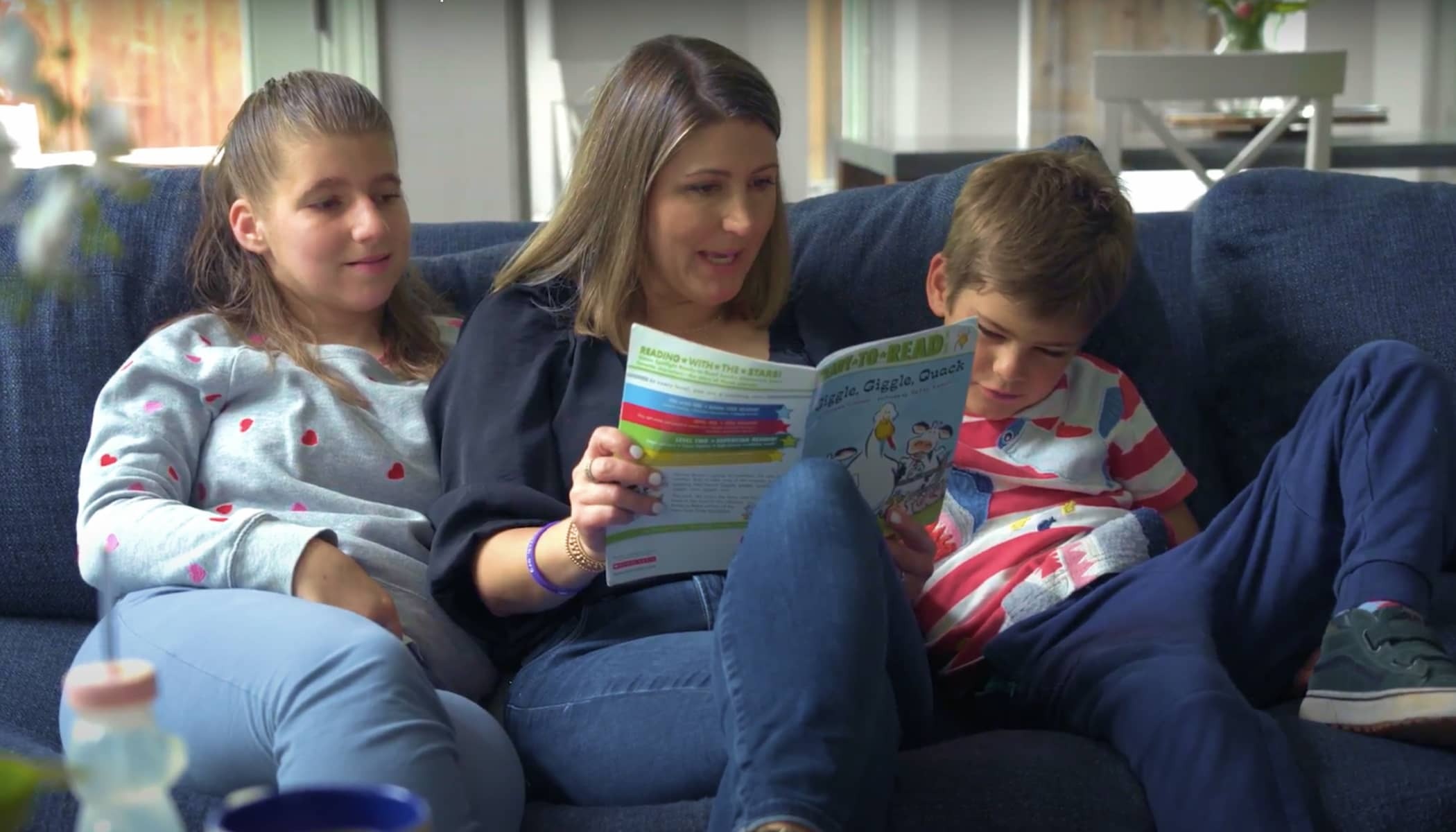 A mother reads to her d aughter and son while sitting on the couch.