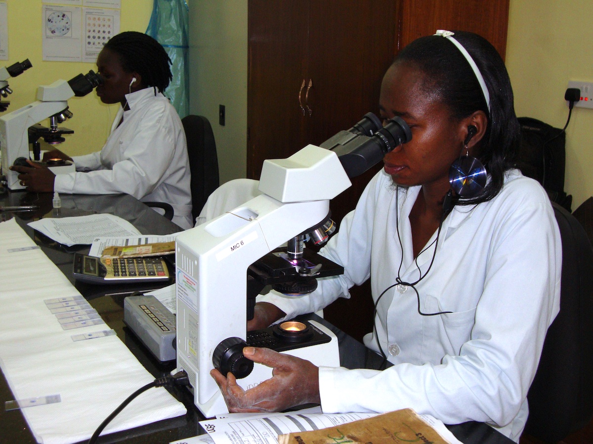two women in white lab coats look into microscopes
