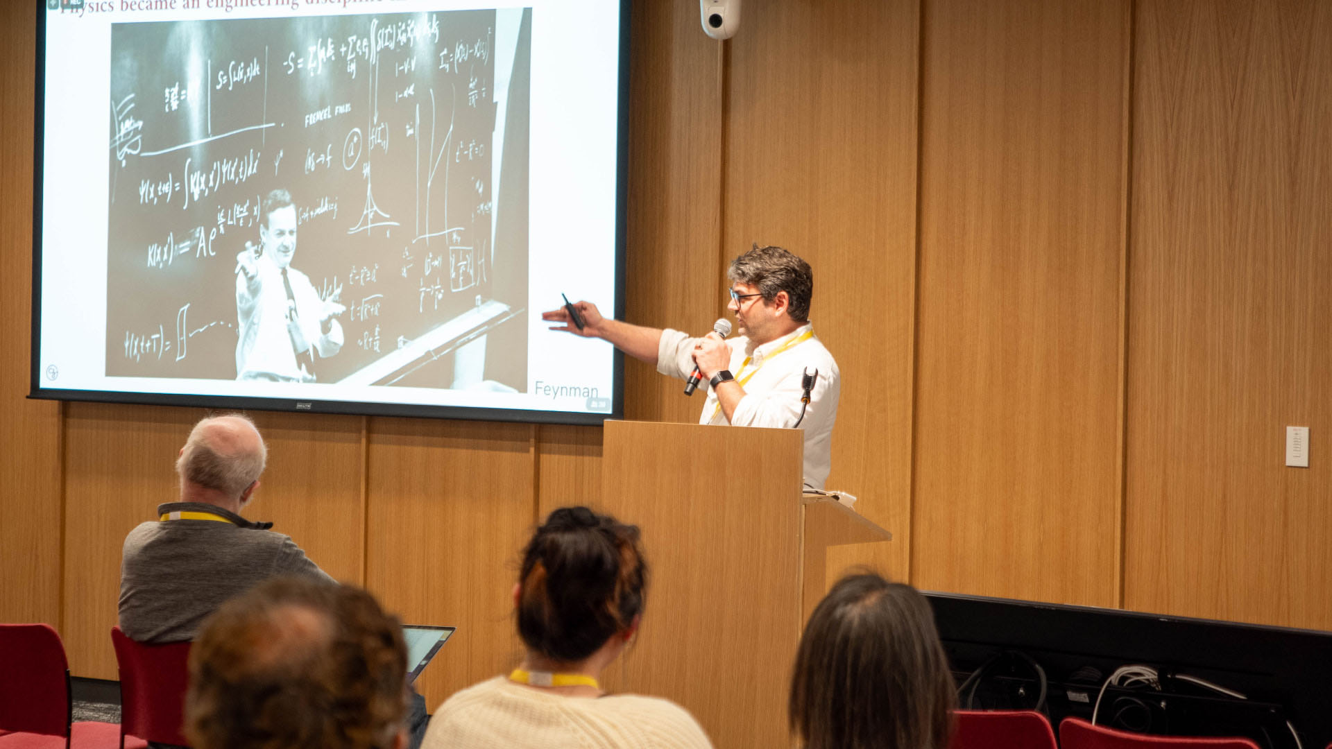 Theofanis Karaletsos is in a white button-up shirt, presenting in front of a podium to an audience.
