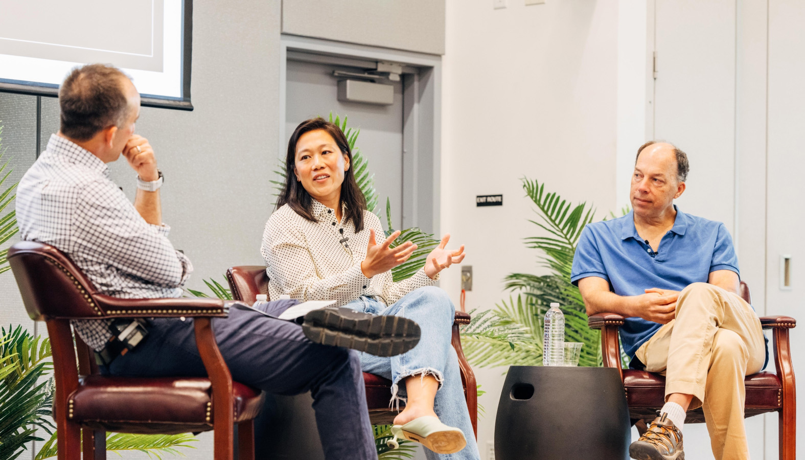Priscilla Chan speaks while gesturing during a panel discussion, with Steve Quake listening beside her and another panelist engaged.