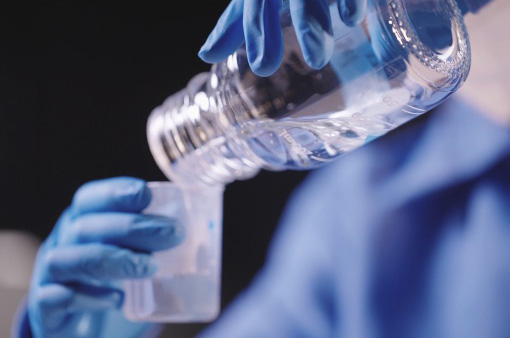 Gloved laboratory researcher pouring solutions from a glass container