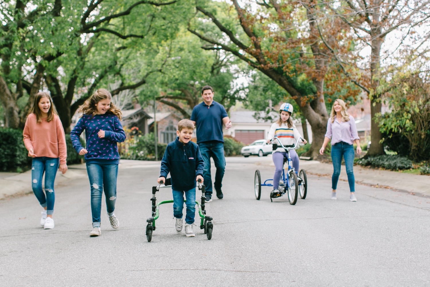 The Nye family walks together outdoors; Colton uses a walker and Tessa rides an adaptive bike, both diagnosed with SLC13A5 Epilepsy.