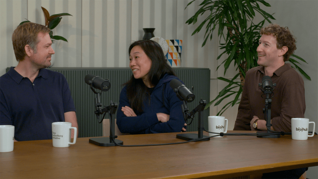 Alex Rives and Biohub Co-Founders Priscilla Chan and Mark Zuckerberg at a conference table with mugs and microhpones.